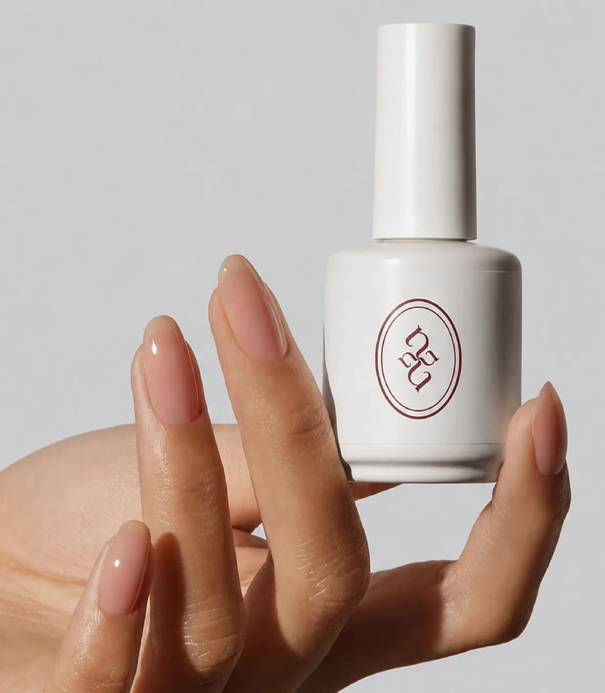 Mano con manicura natural sosteniendo un esmalte con el monograma de Nayeenails
